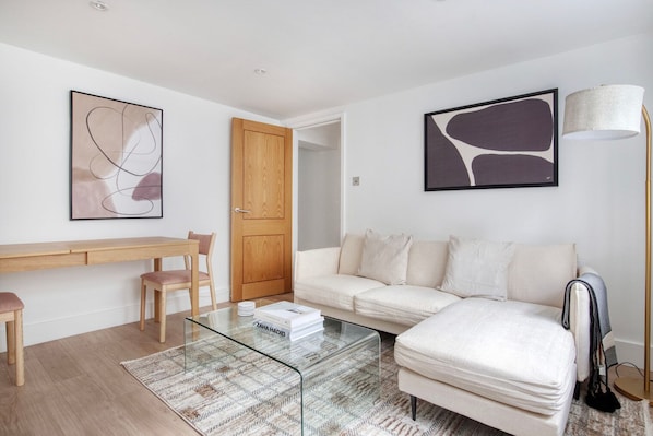 Ein modernes Wohnzimmer mit einem Glastisch, einem weißen Sofa, einer Holztür und abstrakter Wandkunst.