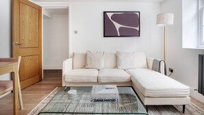 A modern living room with a sectional sofa, a glass coffee table with a book, a wooden door, and a floor lamp. - Convenient Marylebone 1BR, close to Pubs & Restaurants, by Blueground (London)
