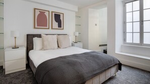 A modern bedroom with a bed, two bedside tables, a window, and two framed artworks on the wall. - Convenient Marylebone 1BR, close to Pubs & Restaurants, by Blueground (London)