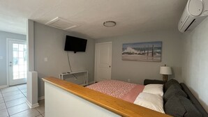 A bedroom with a bed, a TV mounted on the wall, a painting, and a lamp. - Dolphin View House #2 (Eastpoint)
