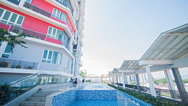 A modern hotel with a swimming pool, multiple balconies, and a covered walkway.