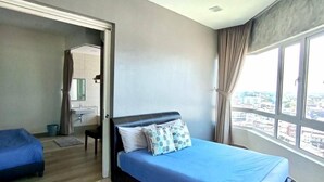 A bedroom with a bed, a bathroom visible through an open door, and a city view through large windows.