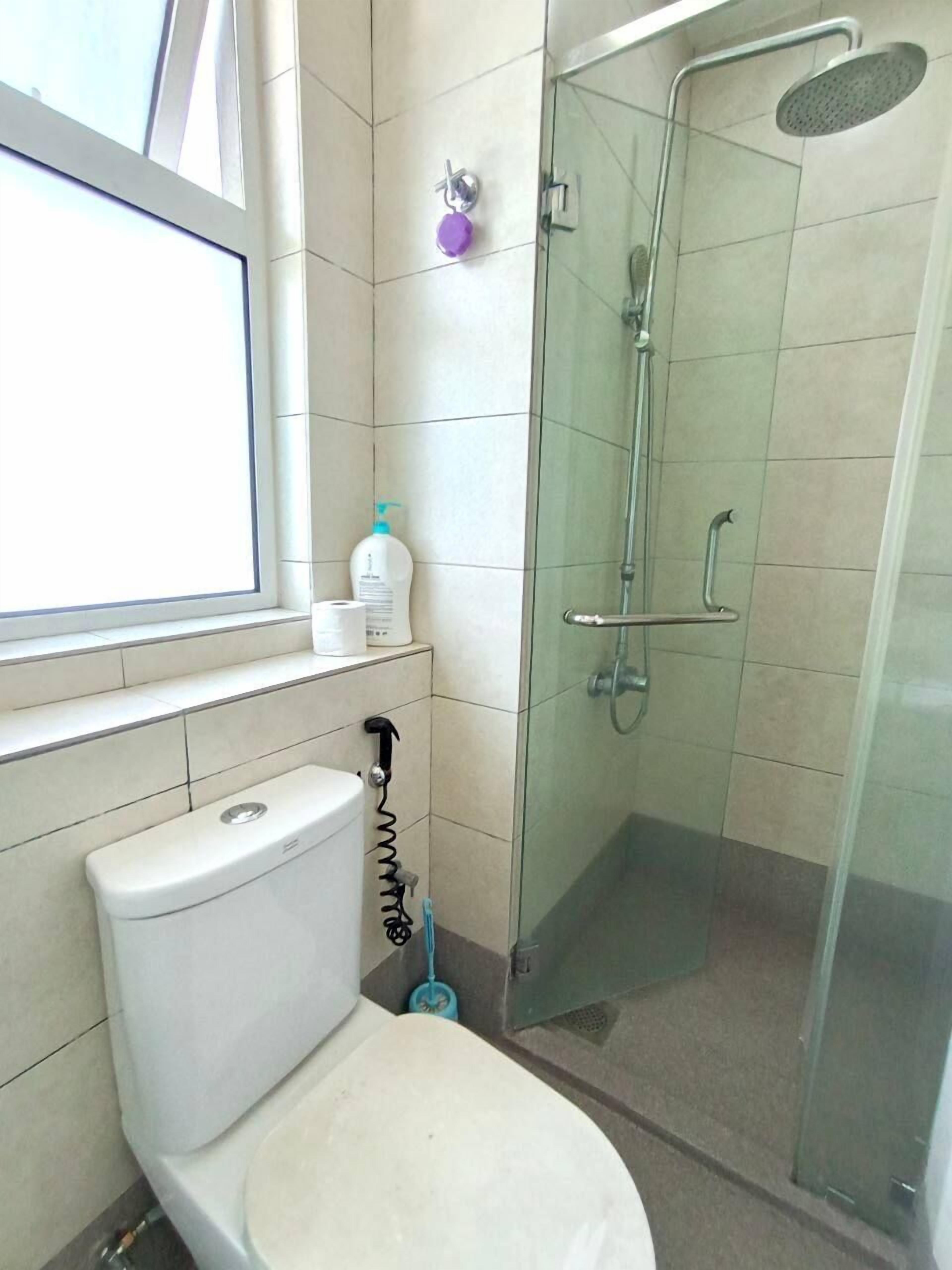 A bathroom with a toilet, a glass shower enclosure, and a window.