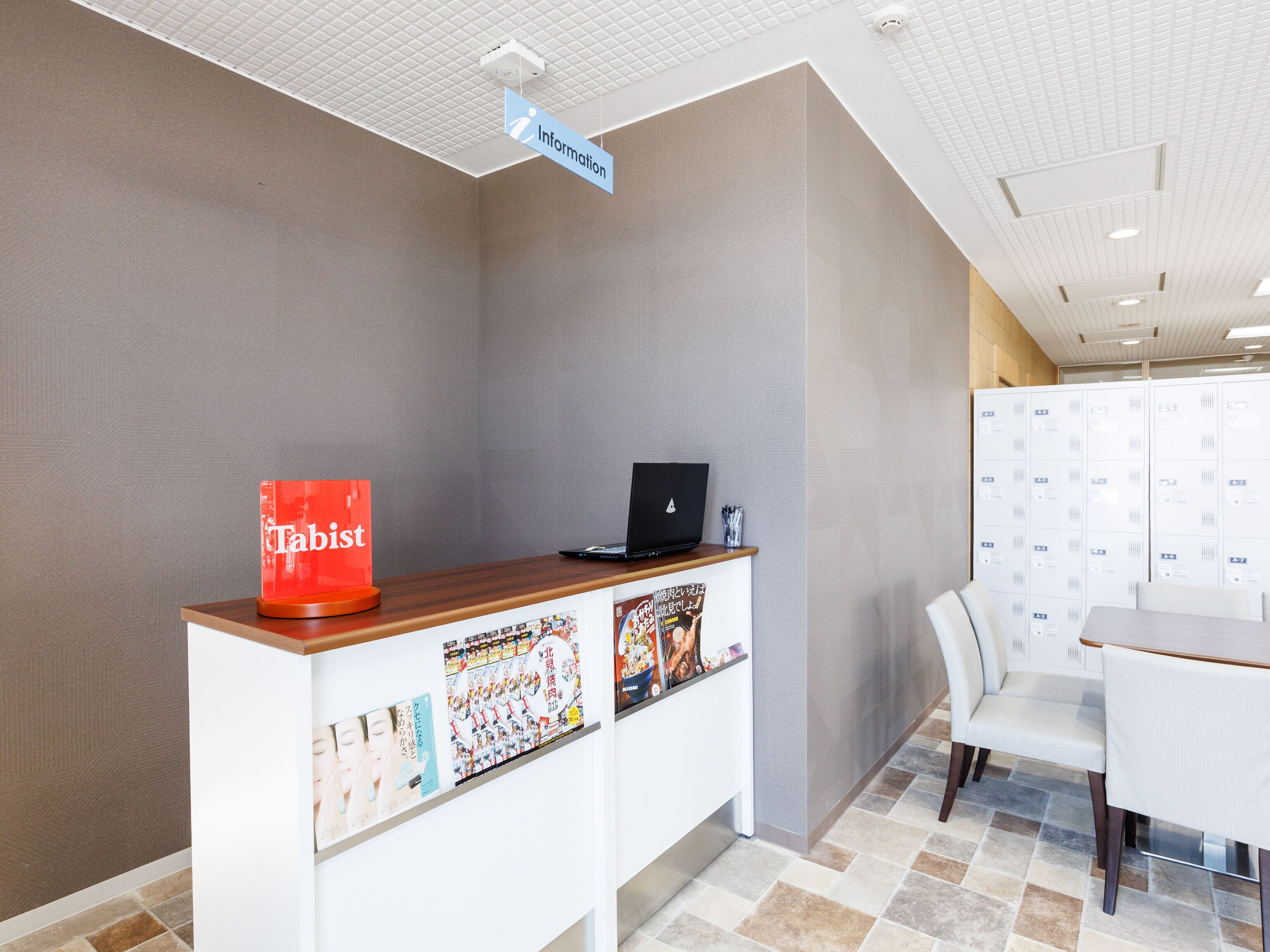 A reception desk with a laptop, a red sign labeled "Tabist," and a wall with lockers.