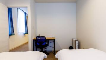 Een hotelkamer met twee bedden, een bureau met stoel, een radiator en een raam met gordijnen.