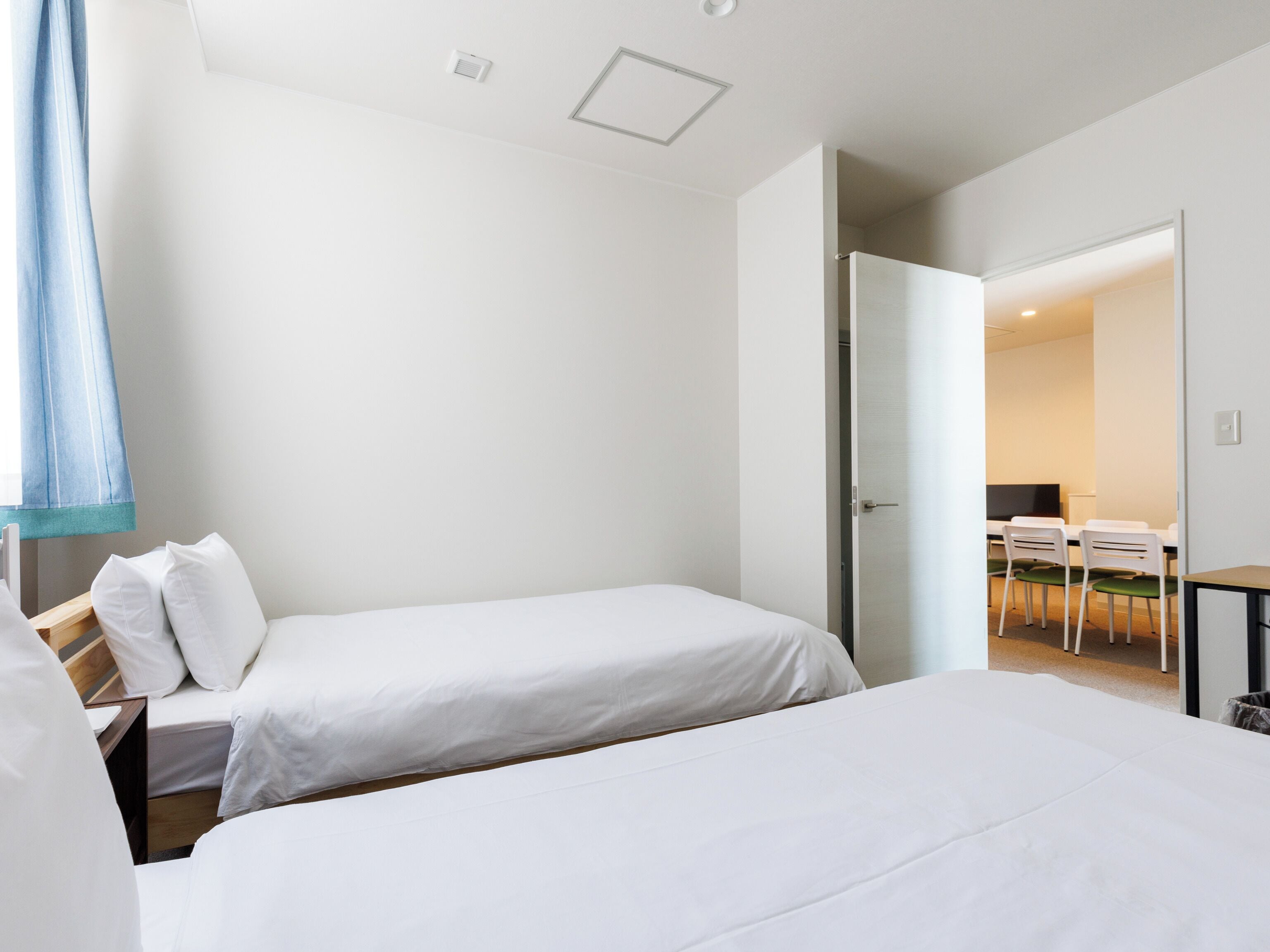 Quarto de hotel moderno com duas camas de solteiro, uma escrivaninha e uma cadeira.