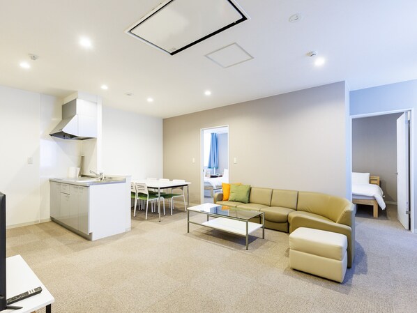 Una habitación de hotel moderna con kitchenette, zona de comedor, sofá y cama.