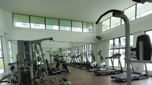 A spacious gym with various exercise equipment, large windows, and a high ceiling.