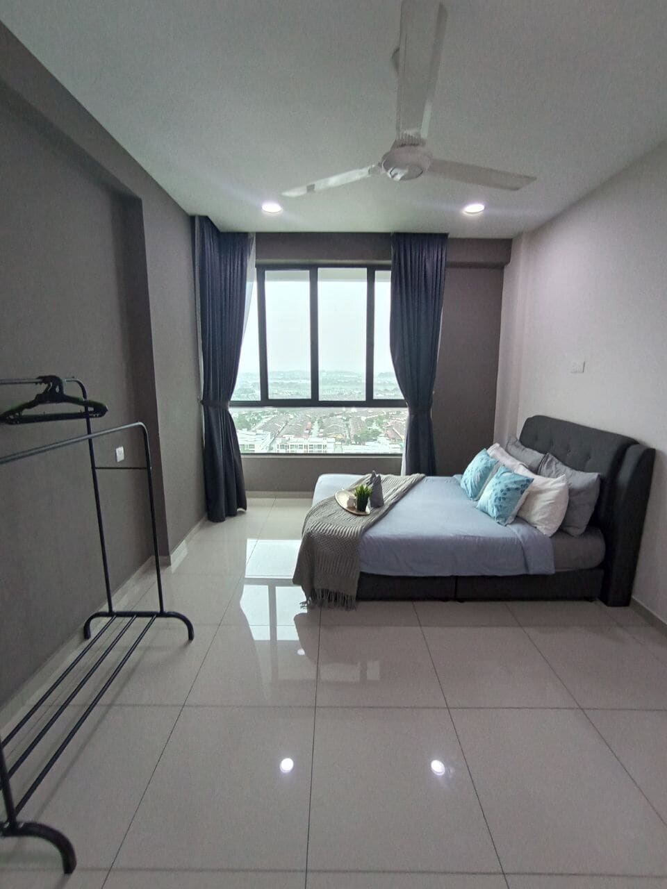 A bedroom with a bed, a ceiling fan, a window with curtains, and a view of the city.