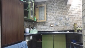 A compact kitchen with green cabinets, a tiled backsplash, and a small trash bin.