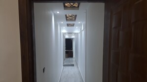 A narrow hallway with a wooden door on the right, recessed lighting, and a ceiling with a geometric design.