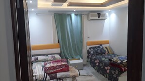 A bedroom with two beds, a window with a green curtain, an air conditioning unit, and a ceiling light fixture.
