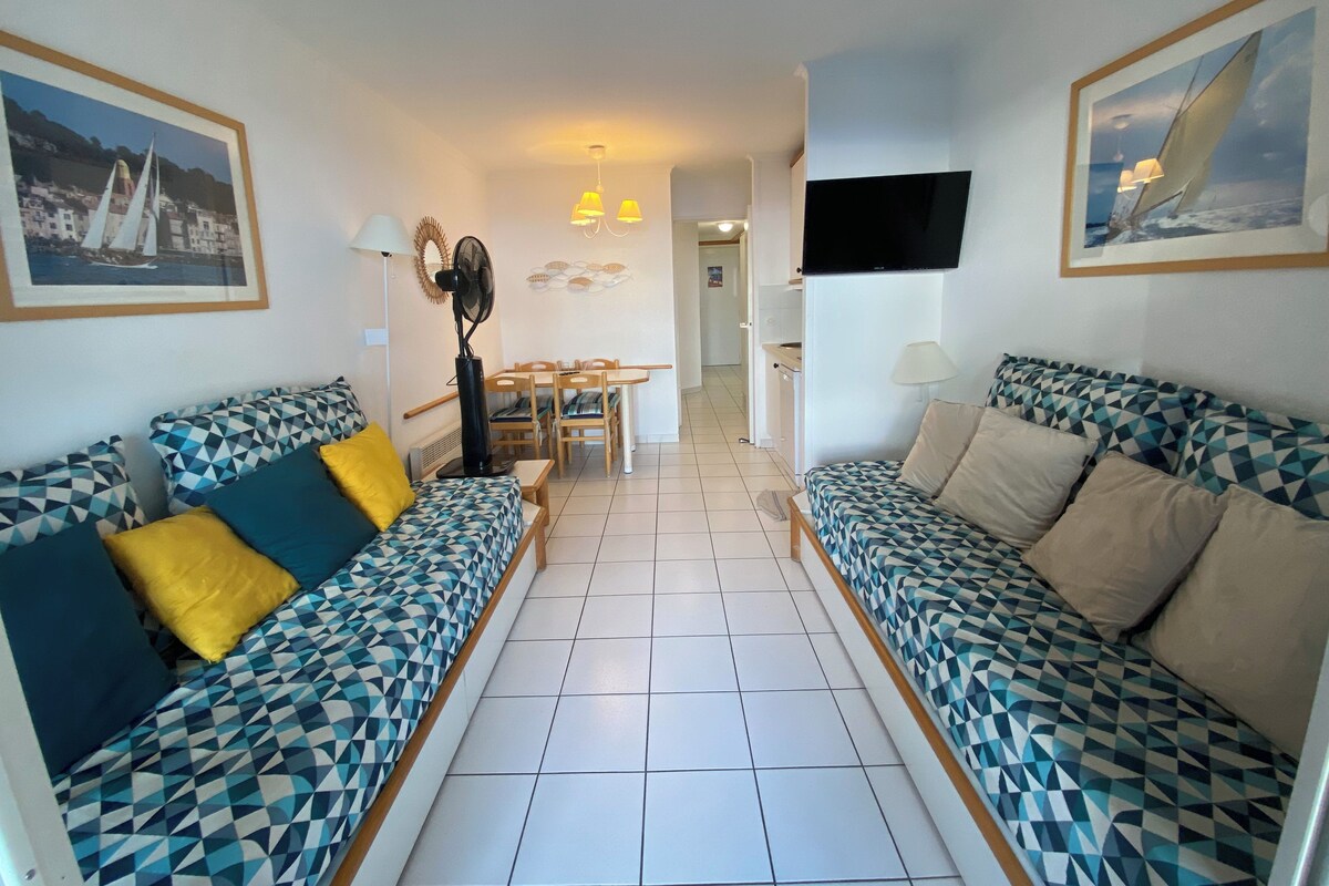 A living room with two patterned sofas, a dining table, and a TV mounted on the wall.