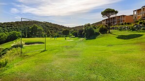 Un terrain de golf avec un poteau de but, un bâtiment doté de balcons et un paysage vallonné.