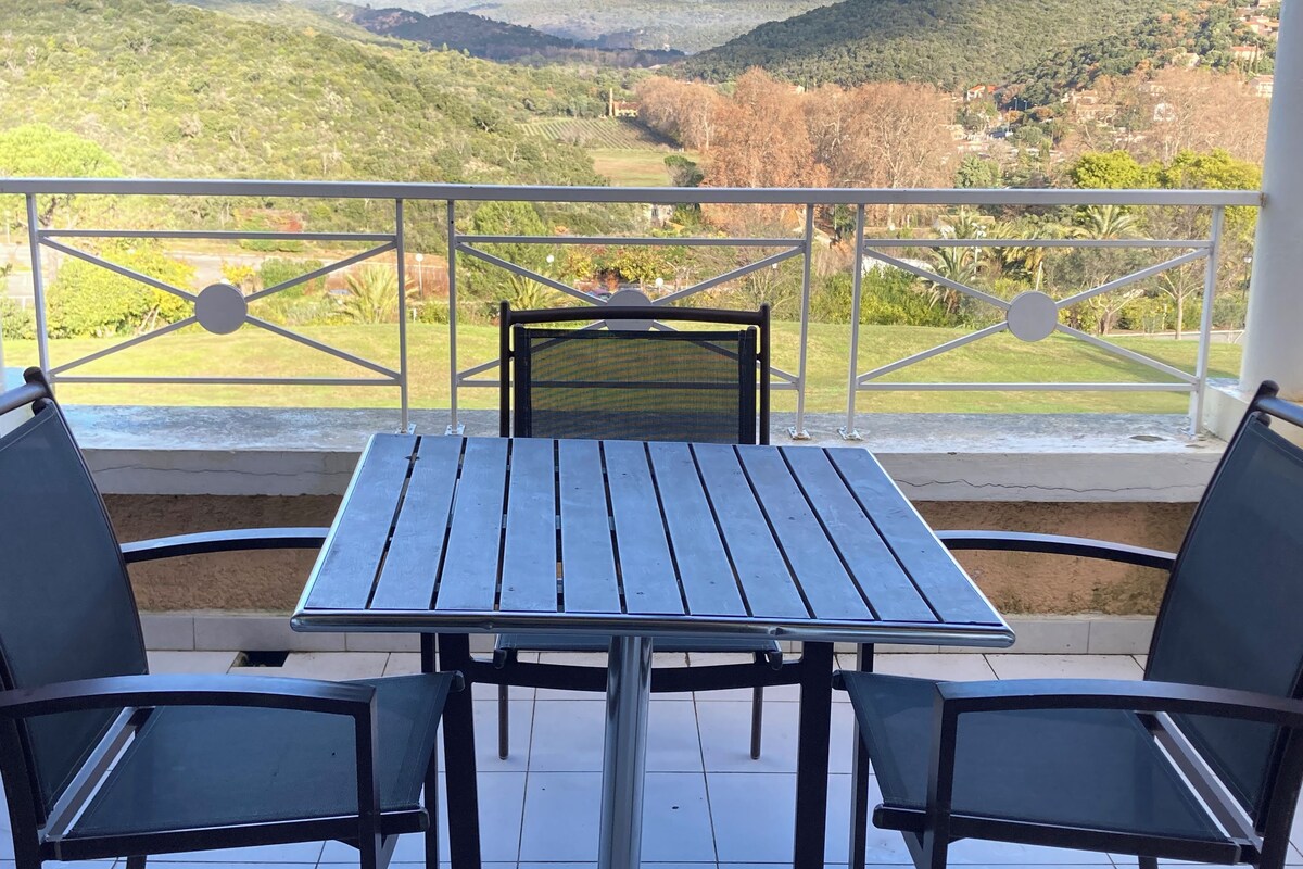Un balcón con mesa y sillas, que ofrece vistas a un paisaje verde con colinas.