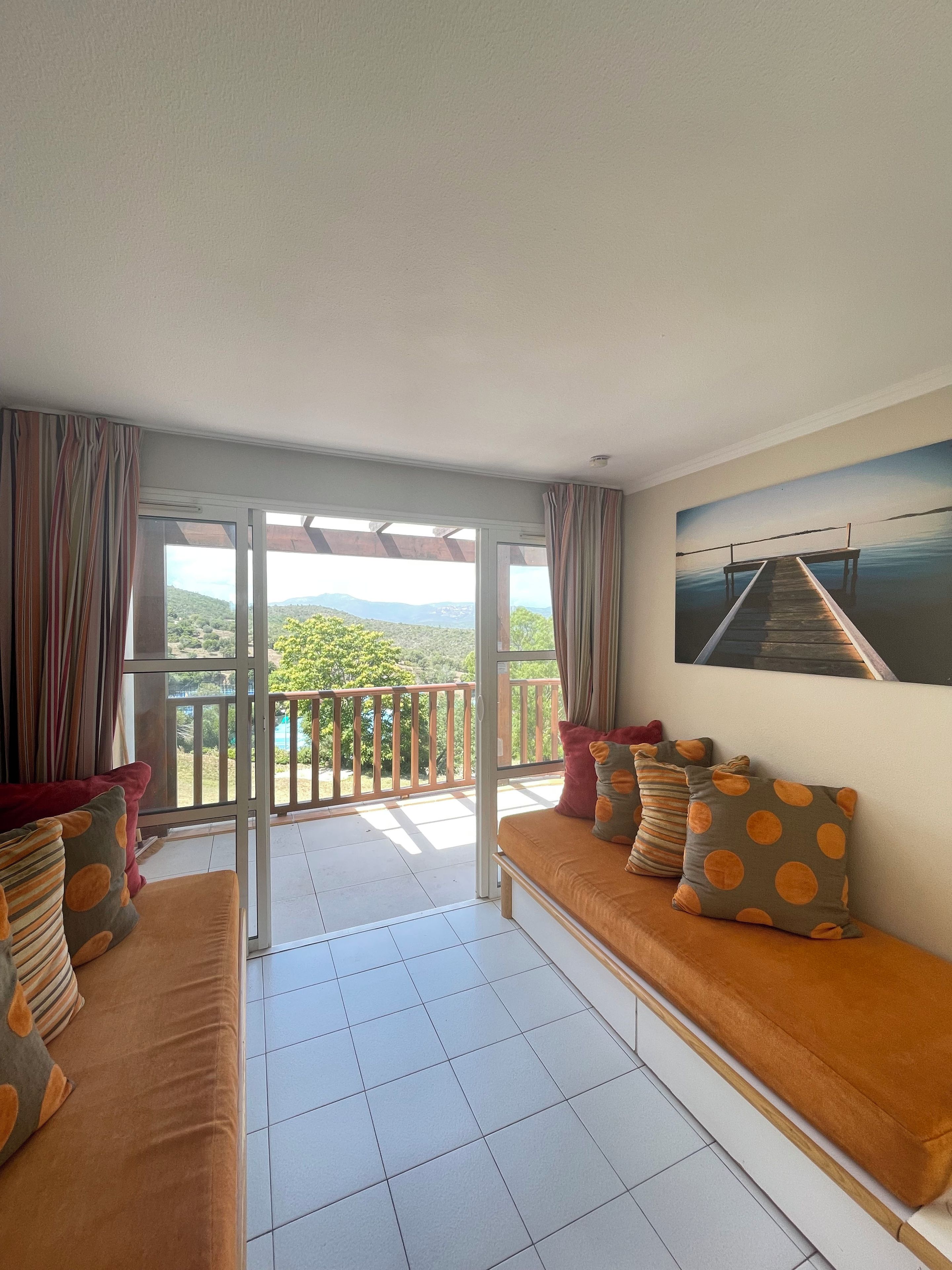 Un balcone con vista su vegetazione e montagne, un divano con cuscini decorati e un quadro appeso al muro.