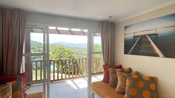 Un balcone con vista su vegetazione e montagne, un divano con cuscini decorati e un quadro appeso al muro.