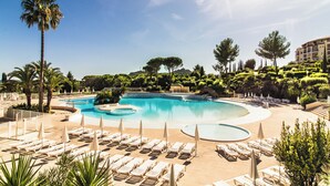A resort pool with sun loungers and umbrellas, surrounded by palm trees and landscaped greenery.