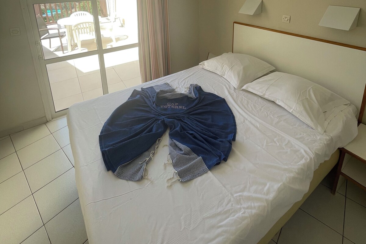 A hotel room with a bed, a view of a balcony with outdoor furniture, and a window with curtains.