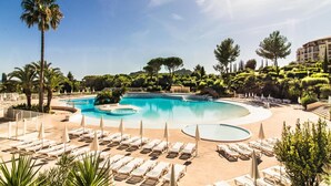 A large, curved swimming pool with lounge chairs and umbrellas, surrounded by palm trees and other greenery.