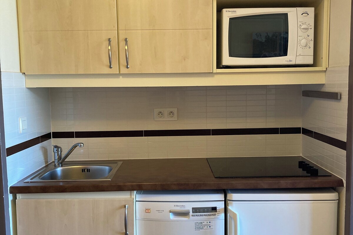 A compact kitchen with wooden cabinets, a microwave, a dishwasher, and a sink.