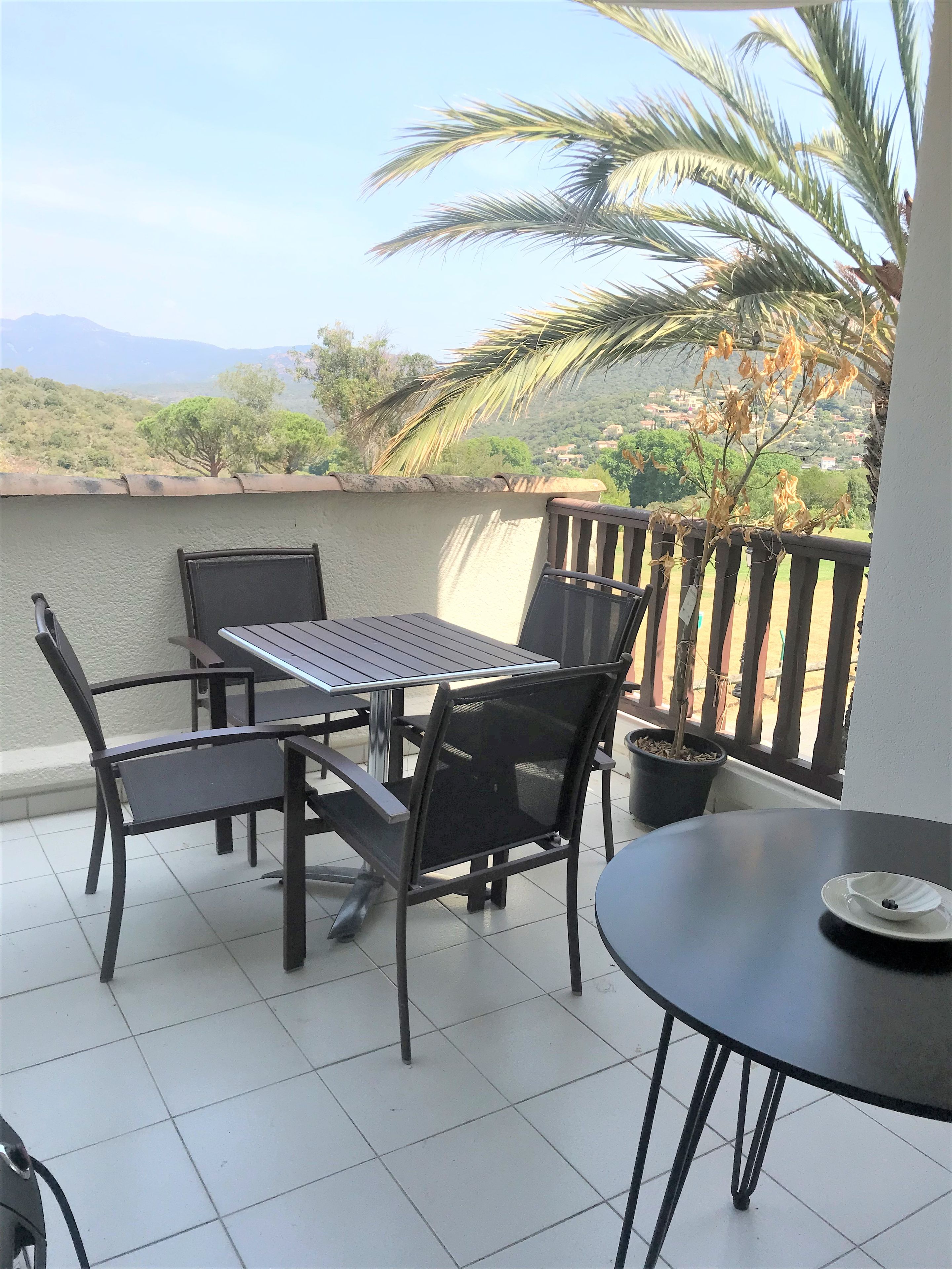 A balcony with a table and chairs, a potted plant, and a view of a hilly landscape.