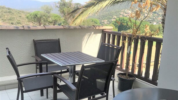 A balcony with a table and chairs, a potted plant, and a view of a hilly landscape.