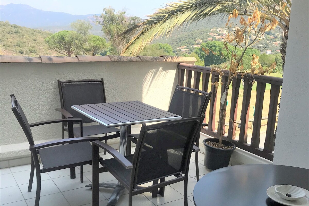 Un balcón con una mesa y sillas, una planta en maceta y vistas a un paisaje montañoso.