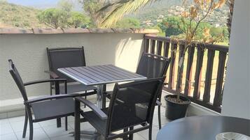 Un balcone con tavolo e sedie, una pianta in vaso e vista su un paesaggio collinare.