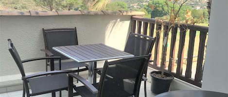 A balcony with a table and chairs, a potted plant, and a view of a hilly landscape.