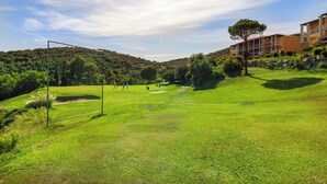 A golf course with a goal post, a building with balconies, and a hilly landscape.