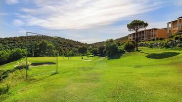 Un campo da golf con un palo di gioco, un edificio con balconi e un paesaggio collinare.