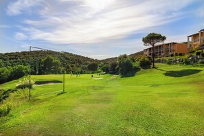 Un campo de golf con un arco de fútbol, un edificio con balcones y un paisaje montañoso.