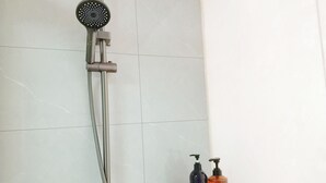 Une douche équipée d’un pommeau de douche à main et d’un robinet mural. On y trouve une étagère avec deux bouteilles de savon.