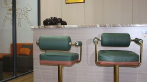 Dos sillones verdes con patas doradas, una placa en la pared y un sofá con cojines anaranjados al fondo.