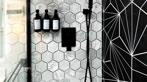 A bathroom with a hexagonal tile wall, a black and white geometric pattern on one side, and a showerhead mounted above a wall-mounted control panel.