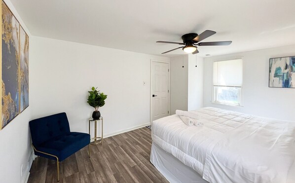 Un dormitorio con una cama, ventilador de techo, ventana y una planta.