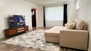 A living room with a beige sofa, a wooden entertainment unit, and a flat-screen TV displaying a video call interface.