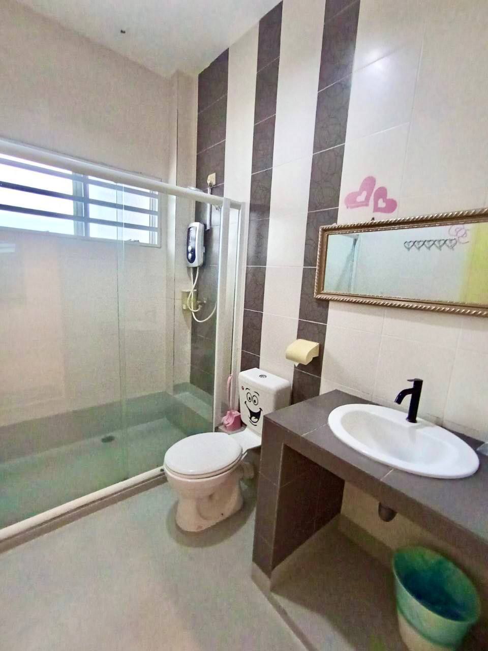Een badkamer met een glazen douchecabine, een toilet met een cartooneske gezichtsuitdrukking en een wastafel met een spiegel erboven.