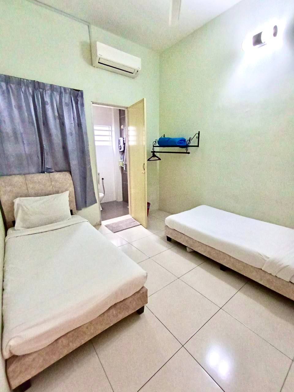 A room with two beds, a hanging air conditioner, a towel rack, and a door leading to a bathroom.