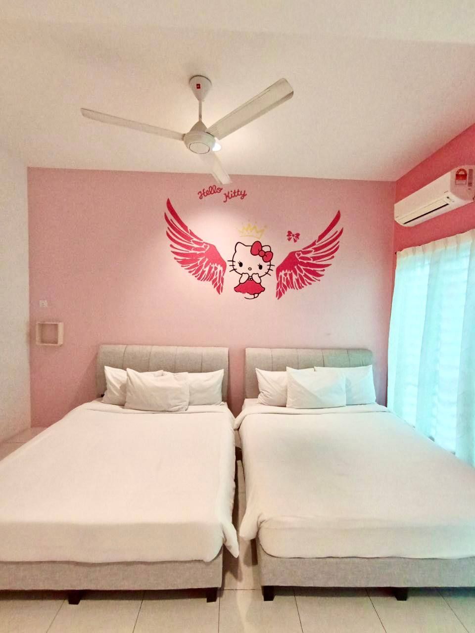 Une chambre d’hôtel avec deux lits, un ventilateur de plafond, un autocollant mural représentant Hello Kitty avec des ailes et un appareil de climatisation.