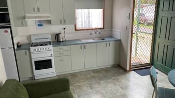 A compact kitchen with white cabinets, a gas stove, a sink, and a window.