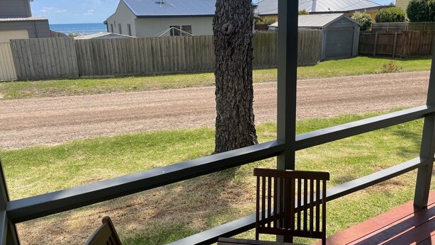 Un espacio al aire libre cubierto con un banco de madera y una mesa, un árbol, y vista a una carretera y casas al fondo.