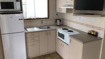 Uma cozinha compacta com geladeira, micro-ondas, fogão, pia e uma televisão instalada acima do balcão.