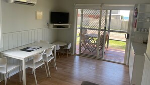 Cocina compacta con comedor, televisor montado en la pared y puerta corrediza de vidrio que da a un patio exterior.