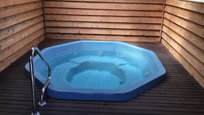 Un jacuzzi en una cabaña de madera con una terraza de madera y un ventanal.