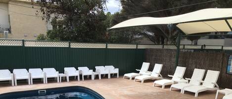 A swimming pool with white lounge chairs and a covered area.