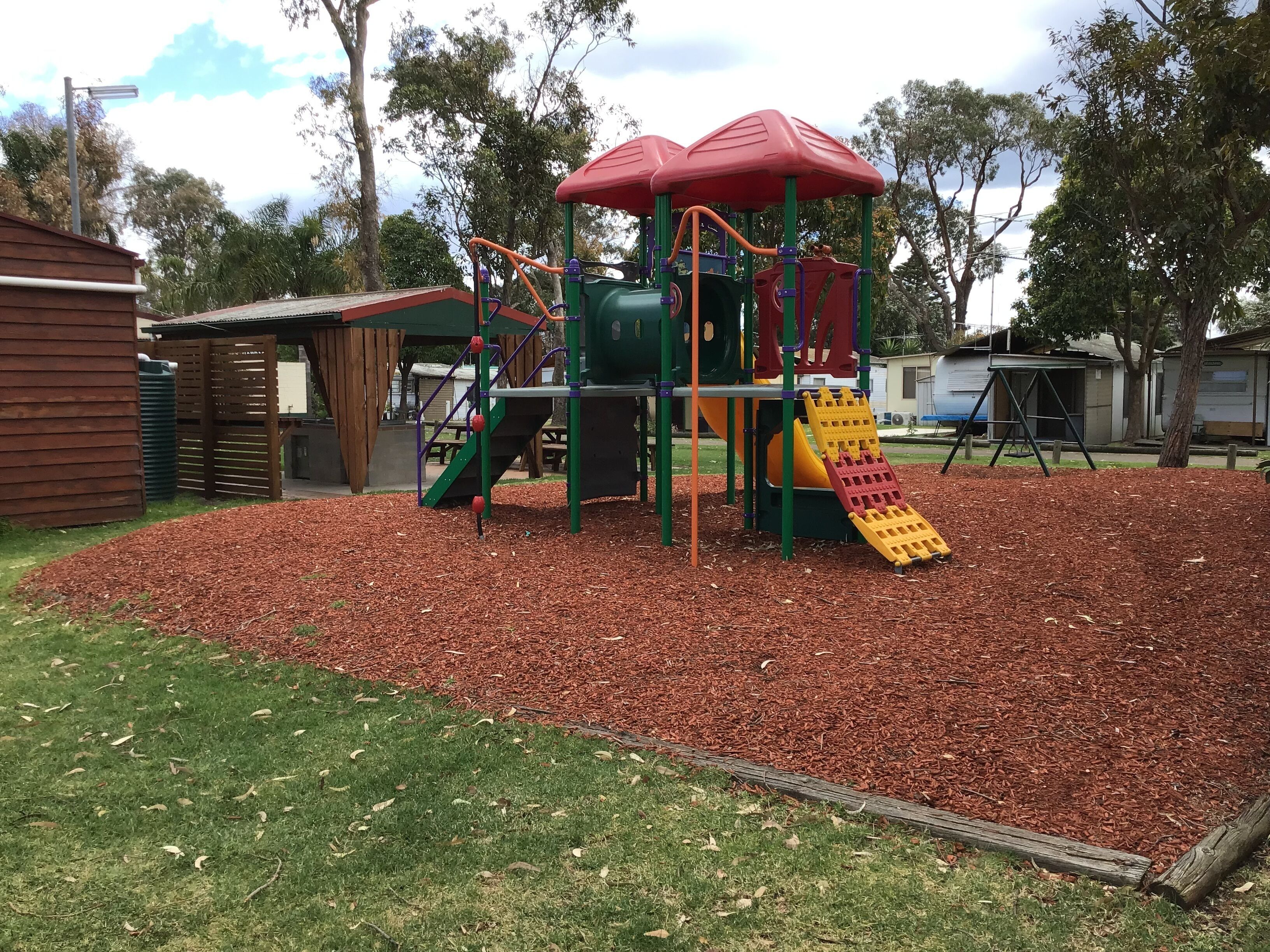 A playground with a slide and climbing structures, surrounded by mulch and grass.