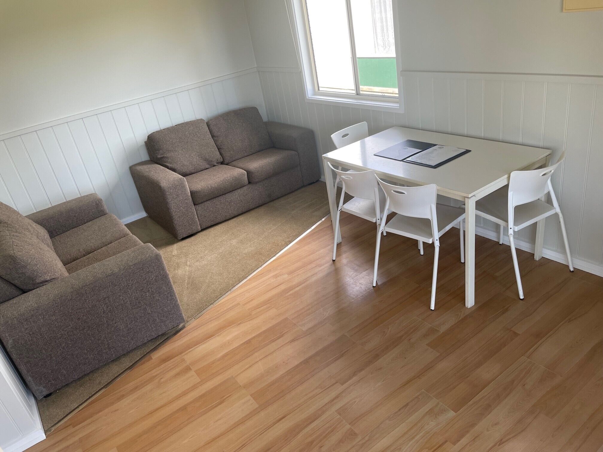 A room with a wooden floor, a white table with four chairs, and a brown sofa.