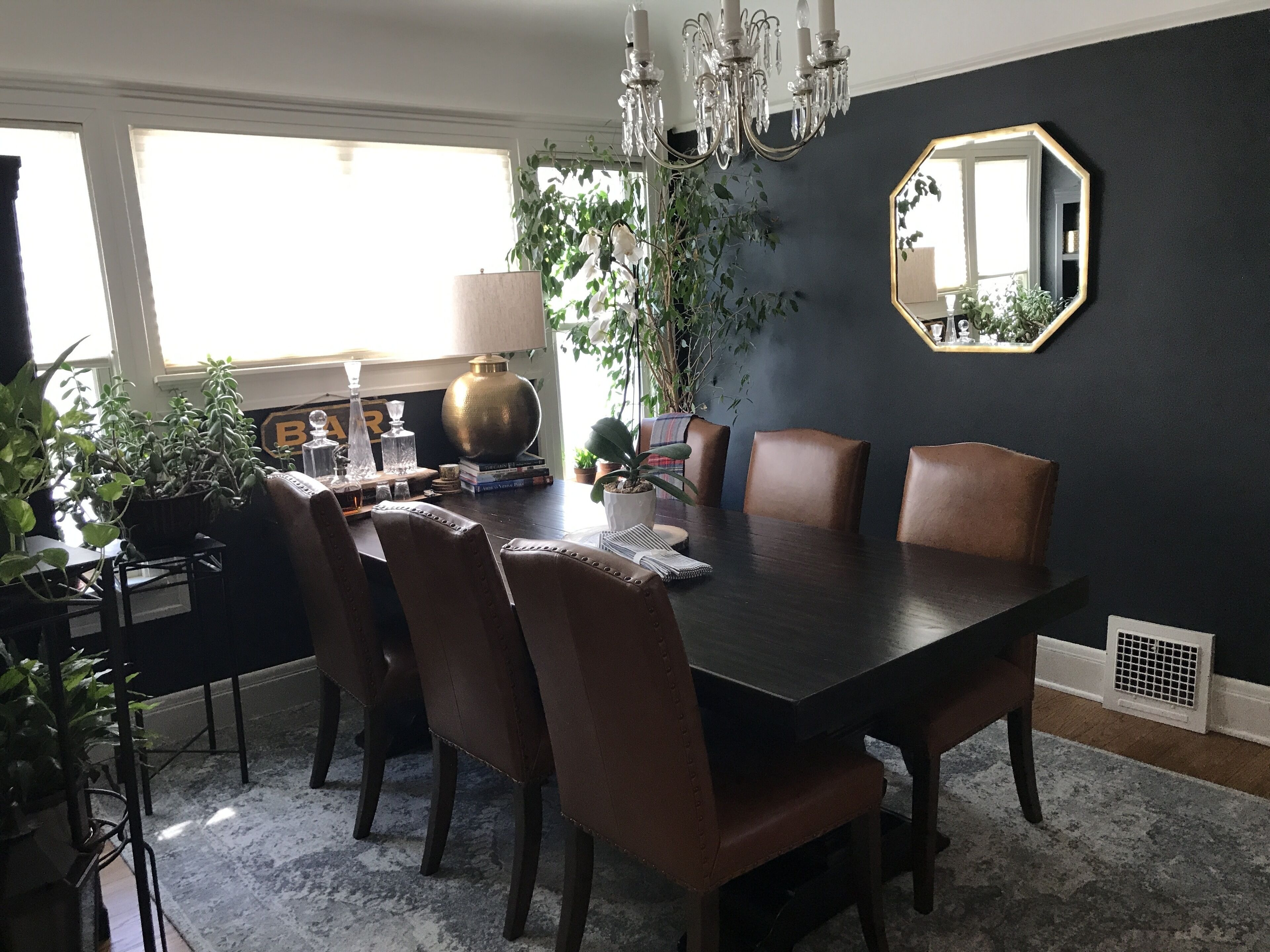 Ein Esszimmer mit einem dunklen Holztisch, sechs braunen Stühlen, einer Kristallleuchtreiter und einem großen Spiegel an der Wand.